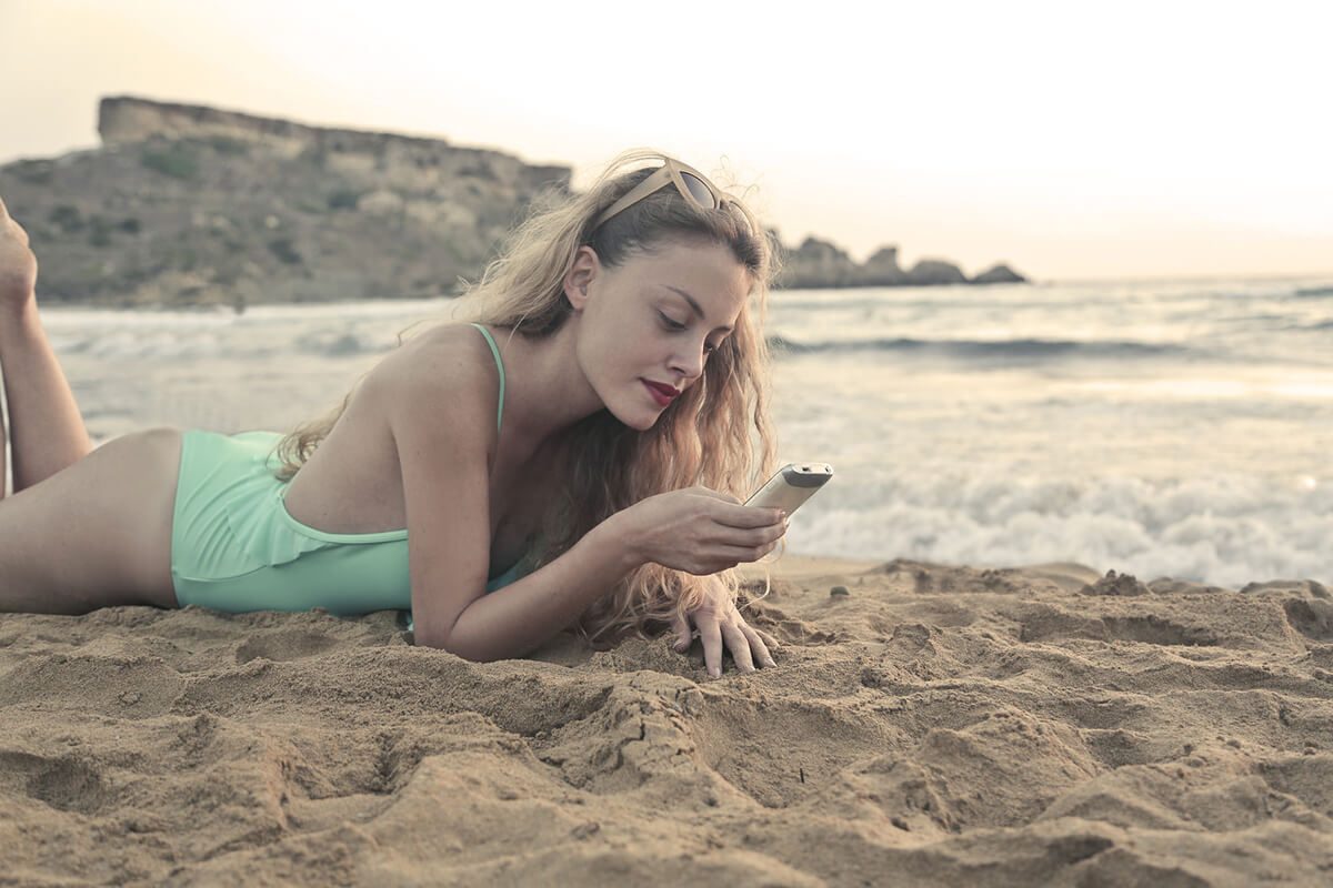 Woman smiling at her phone on the beach
